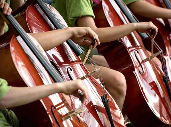 Aufnahme von 3 Kinder in einem Kontrabssorchester, es sind nur die Decken und die Bögen zu sehen.